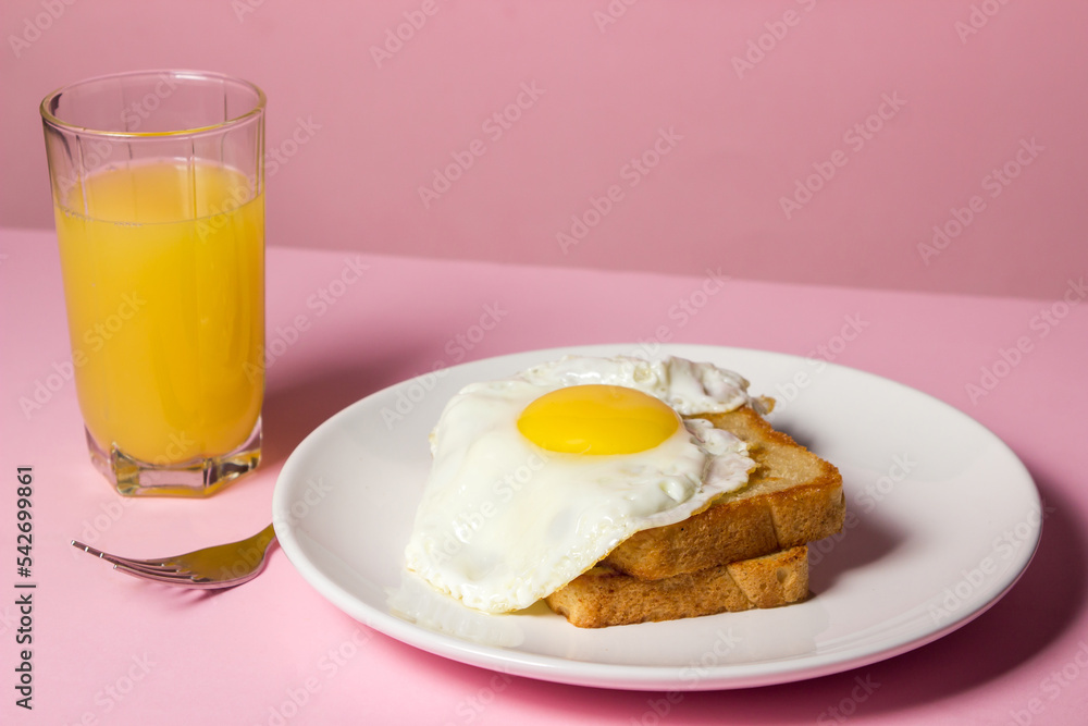Fototapeta premium Fried eggs on a pink background. Breakfast of Fried eggs on fried bread and a glass of juice