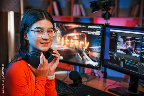 Sitting and smiling. Young beautiful game streamer is indoors with pc