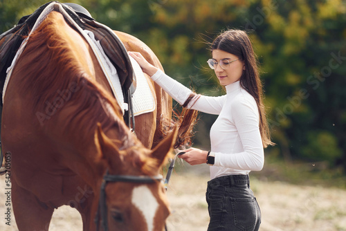 Touching the animal. Young beautiful woman with a horse is outdoors