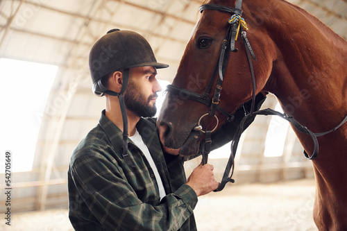 Taking care of animal. Young man with a horse is in the hangar © standret