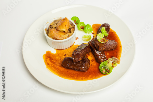 Tasty veal cheeks in red sauce with green. Closeup on a white plate on white background