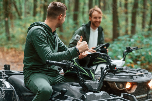 Man showing thumb up. Two male atv riders is in the forest together photo