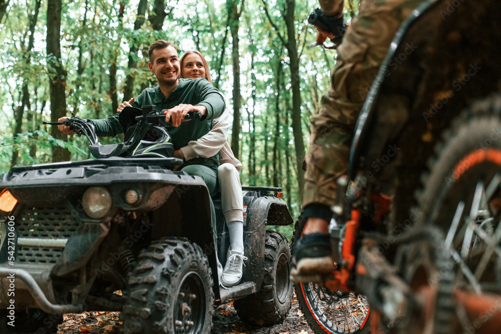 Lovely couple is sitting on the ATV with man on motorcycle in the forest