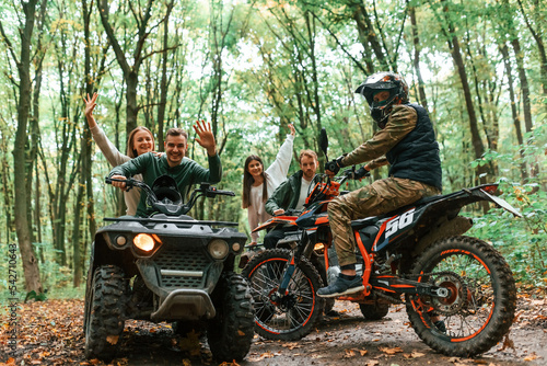 Two couples on ATV with man that is on the bike in the forest that looking at the camera