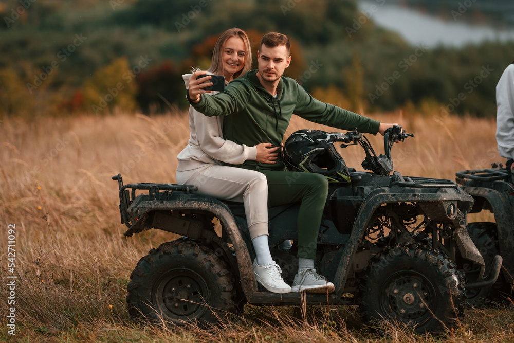 Fototapeta premium Making a selfie. Lovely young couple is with quad bike outdoors on the field