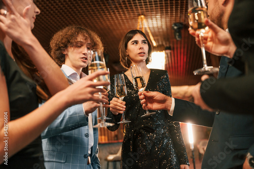 Holding glasses with champagne. Group of people in beautiful elegant clothes are celebrating New Year indoors together