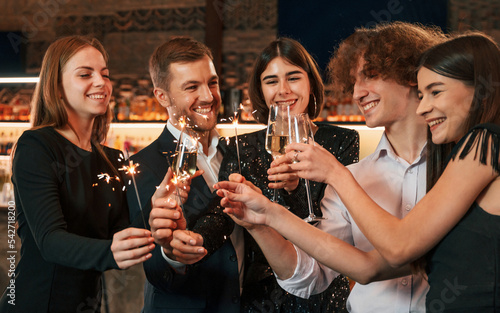 Champagne and sparklers. Group of people in beautiful elegant clothes are celebrating New Year indoors together