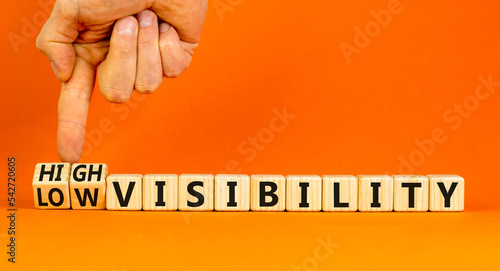 High or low visibility symbol. Concept words High visibility and Low visibility on wooden cubes. Businessman hand. Beautiful orange background. Business high or low visibility concept. Copy space. photo