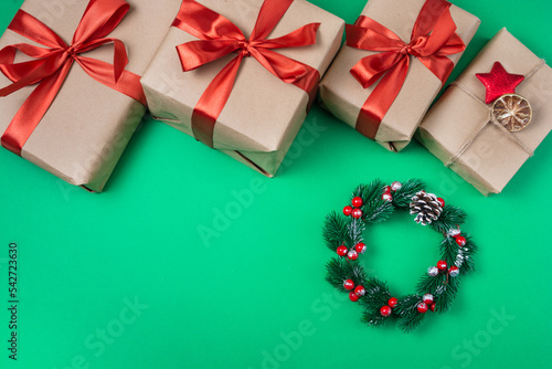 Gifts wrapped in brown paper and a Christmas wreath on a green background. The concept of gifts for Christmas and New Year