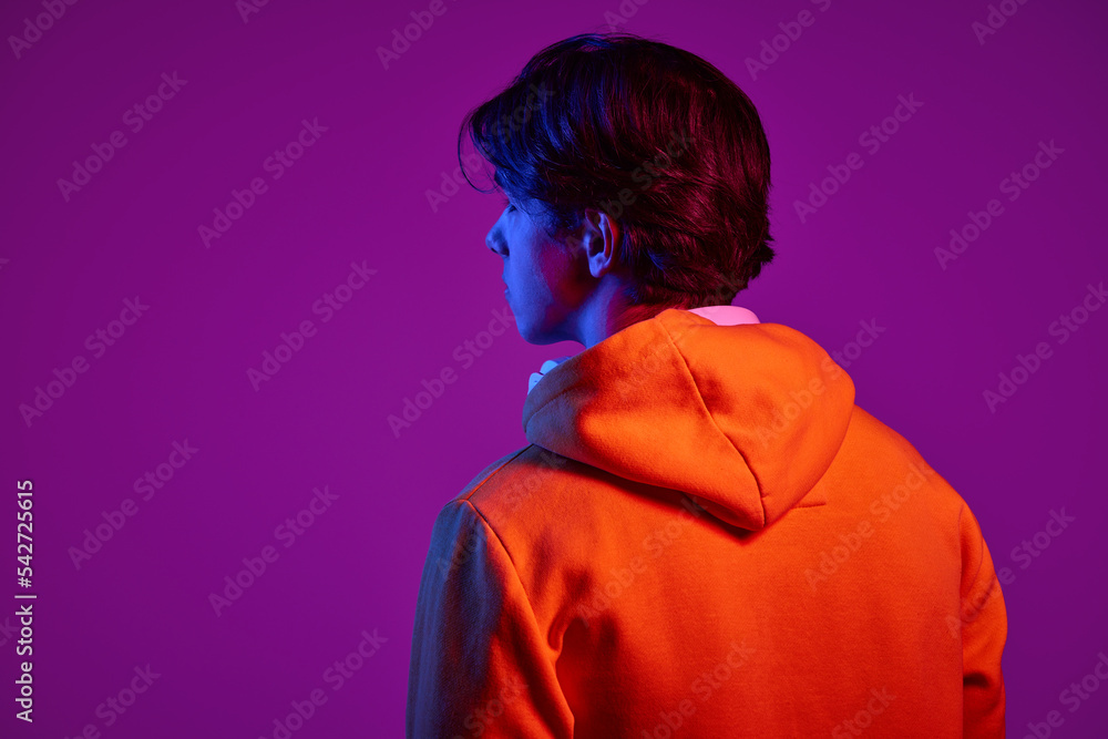 Portrait of young man in casual hoodie posing isolated over purple background in neon light. Back view Portrait of young man in casual hoodie posing isolated over purple background in neon light. Back view