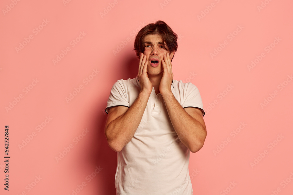 Portrait of young man in casual white T-shirt emotively posing over pink background. Making wrong, failed Portrait of young man in casual white T-shirt emotively posing over pink background. Making wrong, failed