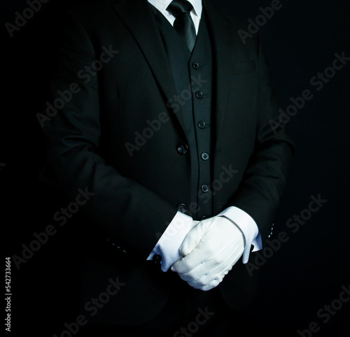Portrait of Butler in Dark Suit and White Gloves Standing at Attention on Black Background. Service Industry and Professional Hospitality.
