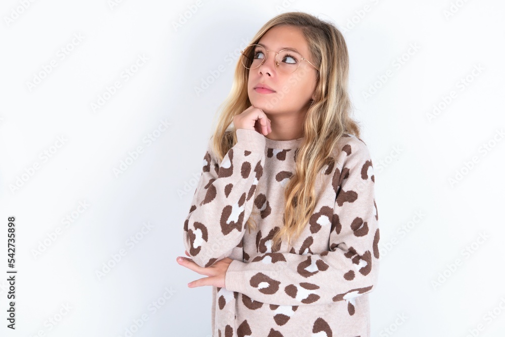 Portrait of thoughtful little caucasian kid girl wearing animal print sweater keeps hand under chin, looks away trying to remember something or listens something with interest. Youth concept. Portrait of thoughtful little caucasian kid girl wearing animal print sweater keeps hand under chin, looks away trying to remember something or listens something with interest. Youth concept.