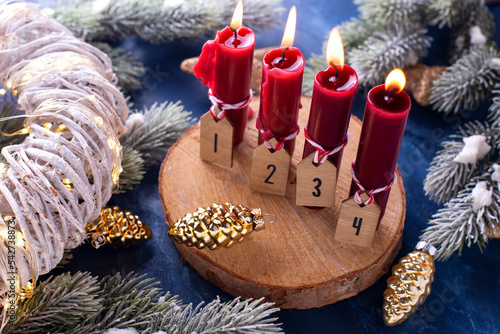 Red advent  Christmas composition. Red burning candles,  branches of fur trees and part of white wreath  on  blue  textured background. Still life photo