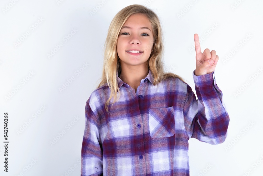 beautiful caucasian teen girl wearing plaid purple shirt over white wall showing and pointing up with finger number one while smiling confident and happy. beautiful caucasian teen girl wearing plaid purple shirt over white wall showing and pointing up with finger number one while smiling confident and happy.