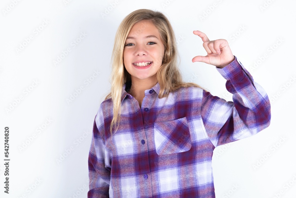 beautiful caucasian teen girl wearing plaid purple shirt over white wall smiling and confident gesturing with hand doing small size sign with fingers looking and the camera. Measure concept beautiful caucasian teen girl wearing plaid purple shirt over white wall smiling and confident gesturing with hand doing small size sign with fingers looking and the camera. Measure concept