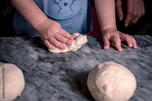 Kid's hands dough for pizza on the marble table.