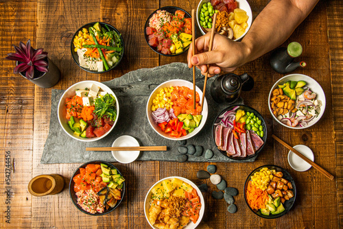 A person's arm with chopsticks among a pile of bowls of fresh and healthy food