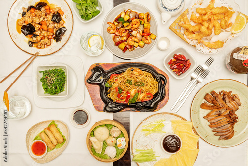 Set of mainly Asian and Chinese dishes, udon noodles with vegetables and shrimp, Vietnamese rolls, chicken with shiitake mushrooms, spicy shrimp with vegetables, and shrimp tempura