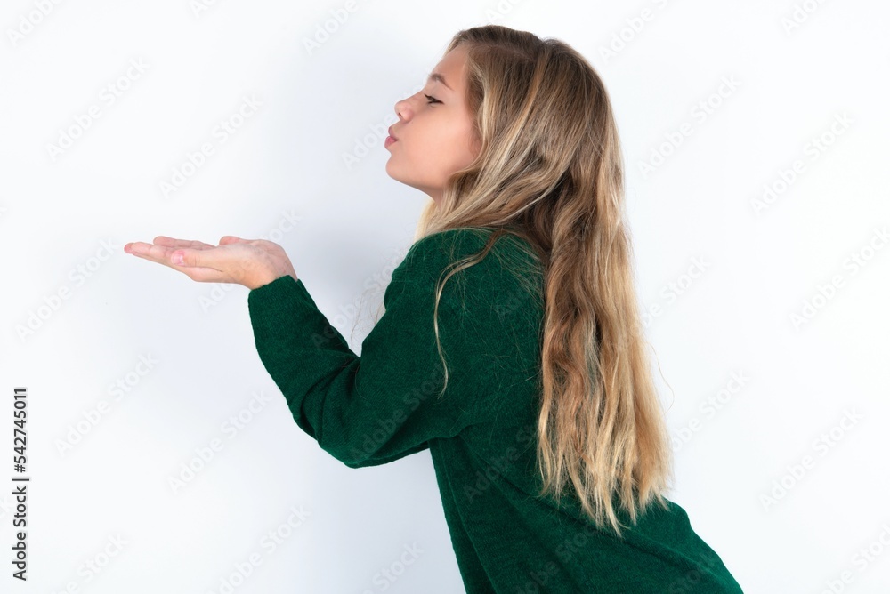 Profile side view, portrait of attractive beautiful caucasian teen girl wearing green knitted sweater over white wall sending air kiss Profile side view, portrait of attractive beautiful caucasian teen girl wearing green knitted sweater over white wall sending air kiss