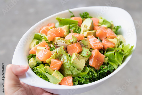 Salmon salad with green leaves and avocado on oval white bowl.