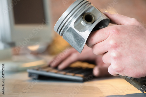 Car service worker with a engine piston in hand orders a car spare parts through the internet with the computer concept.