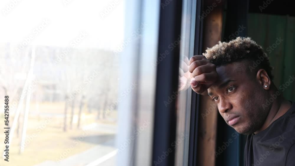 Brooding African guy in a black T-shirt is standing by the window ...