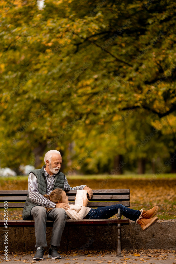 Fototapeta premium Grandfather spending time with his granddaughter on bench in park on autumn day