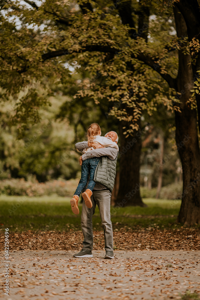 Grandfather spending time with his granddaughter in park on autumn day Grandfather spending time with his granddaughter in park on autumn day