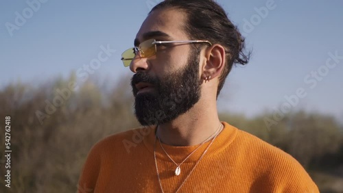 Slow-motion shot of a white young male with beard eyeglasss orange blouse necklace with a pendant photo