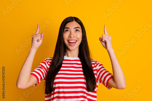 Photo of impressed sweet young lady wear red clothes looking pointing up empty space isolated yellow color background