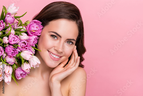 Photo of pretty cute nude lady wear nothing holding tulips bloom hand cheek empty space isolated pink color background