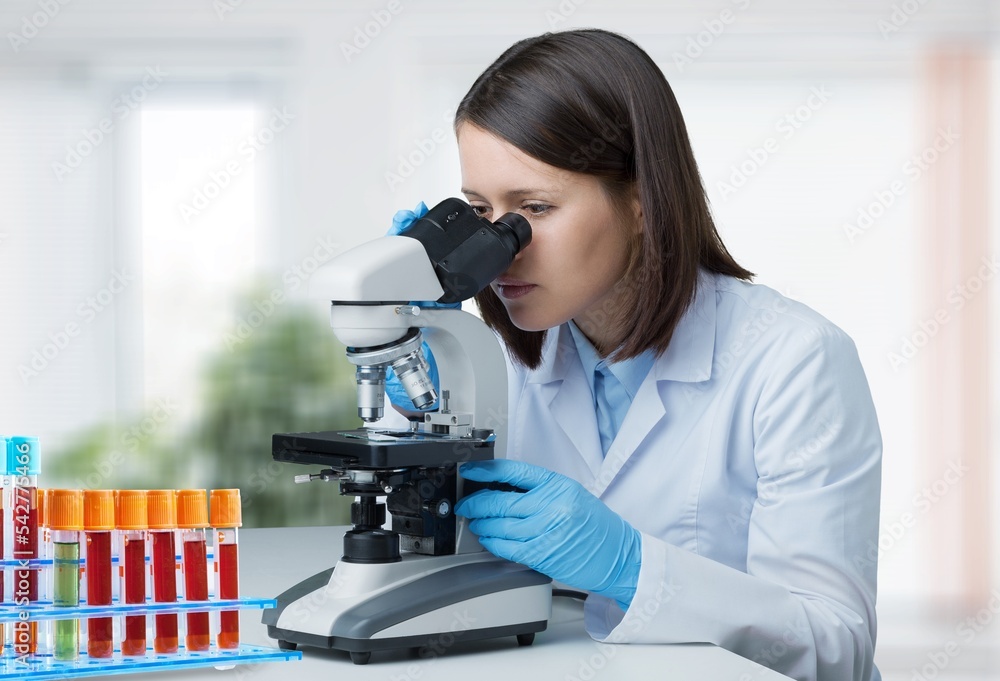 Young doctor with sample tube and microscope in lab Young doctor with sample tube and microscope in lab