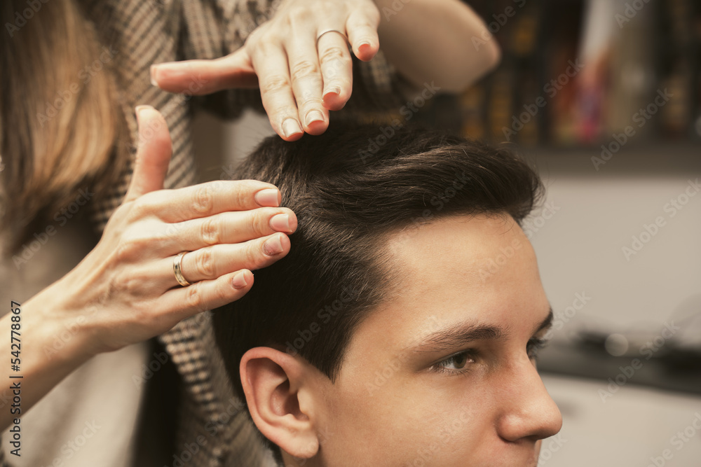 Naklejka premium Young man getting a modern haircut. Hair salon master does hair styling client at barber shop. Men's fashion and style. Hair care, beauty industry, barber concept. Barber shop men hairstyle