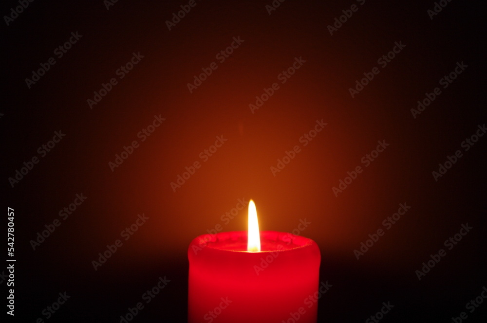 A red candle on a dark background, emphasizing the flame A red candle on a dark background, emphasizing the flame