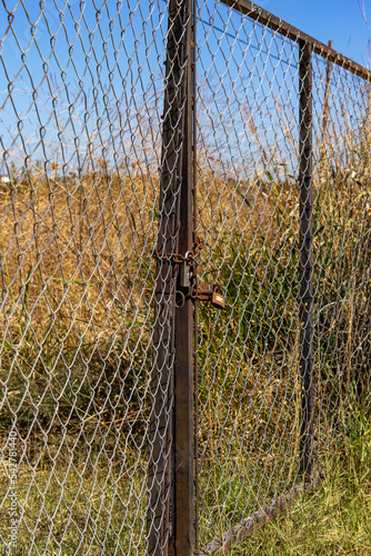 A closed gate in a chain-link fence in a field. Close-up.