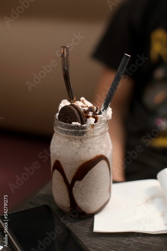 Vertical shot of a cookie milkshake in a glass jar with a straw on the blurred background