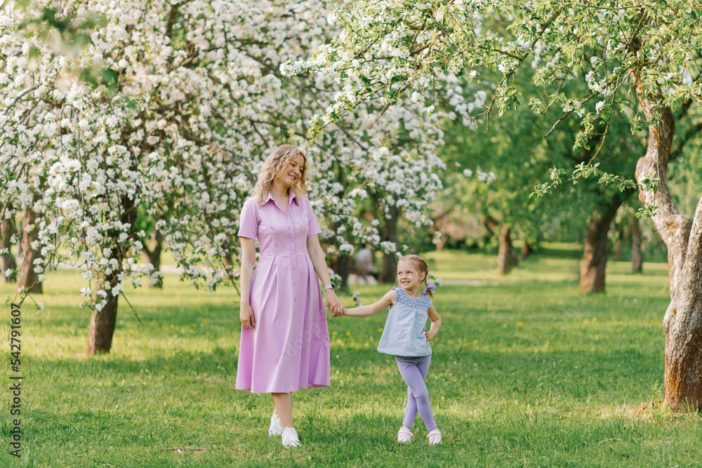 Mom and little daughter are walking through a blooming spring garden Mom and little daughter are walking through a blooming spring garden