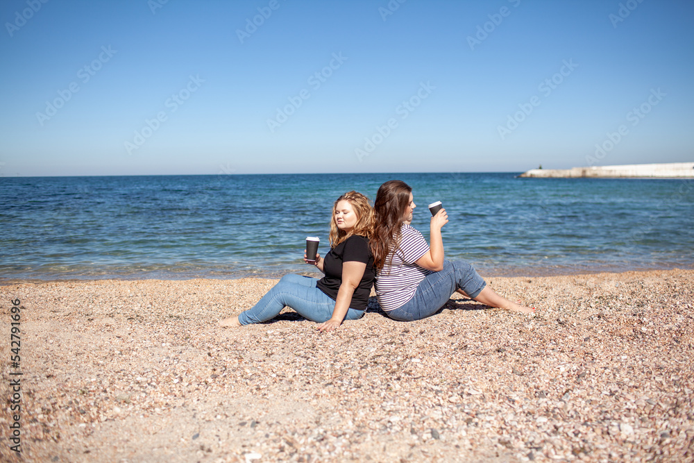 Two plus size female friends walking in the beach, resting and enjoy the moment to be alone and meditate near the sea or ocean in the beach. Overweight women wearing dress
