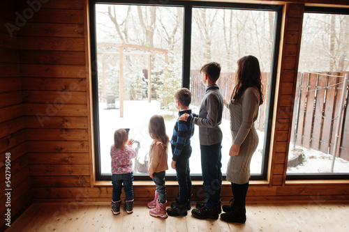 Mother and four kids in modern wooden house against large window.