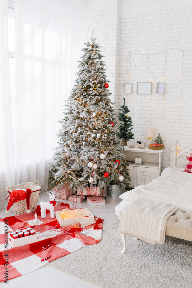 Interior of the bedroom is white and red with a large Christmas tree by the window and bed