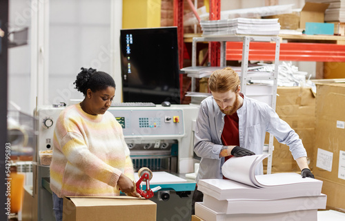 Portrait of two workers opening boxes with paper in industrial print shop  copy space