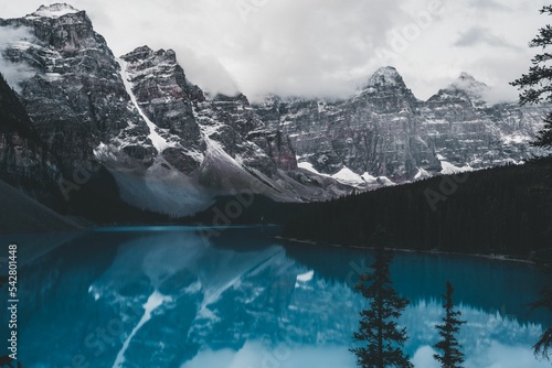 Long shot of lake moraine reflecting surrounding trees and snow-capped mountains.