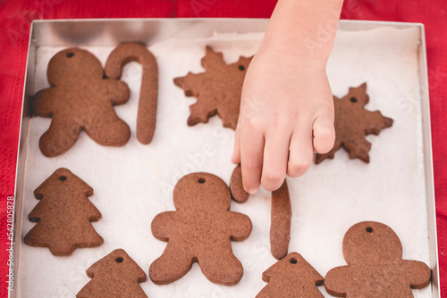 Overhead view of a child's hand reaching for a freshly baked homemade s snowflake gingerbread cookie photo