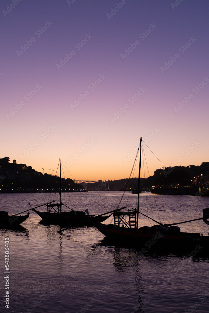 Sailing boats on the edge of the shore of the Douro River in Porto, Portugal at purple dusk summer night scene