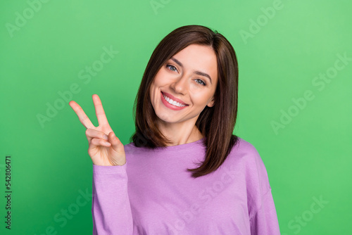 Closeup photo of young smiling cute woman showing v-sign hello friends looking you isolated on green color background