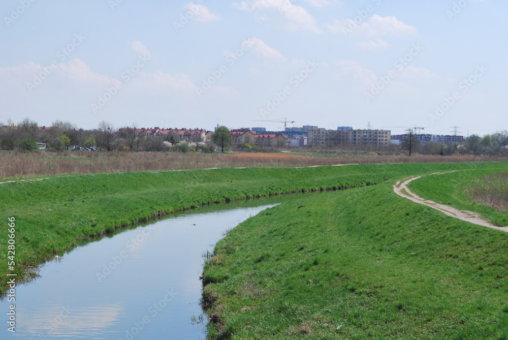 a river flowing in an arc, grassy embankments, plain, distant buildings a river flowing in an arc, grassy embankments, plain, distant buildings