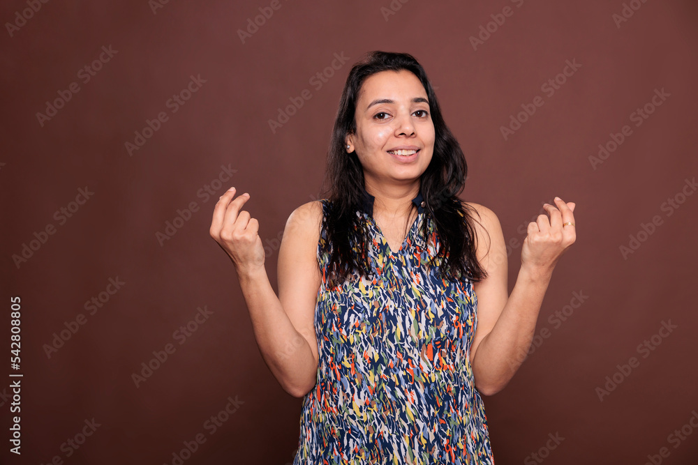Fototapeta premium Smiling indian woman showing money gesture portrait, looking at camera. Profit, earnings, cash concept, positive wealthy lady with cheerful facial expression, front view studio medium shot