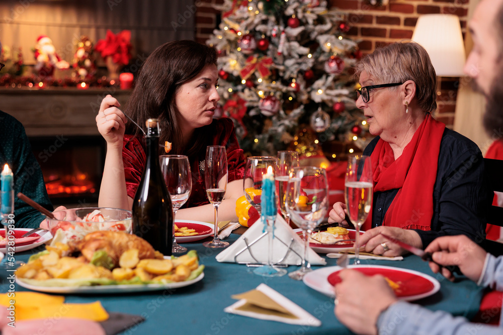 Woman chatting with mom at family christmas celebration, talking at festive dinner table at home party. People eating traditional xmas food, having conversation, celebrating holidays