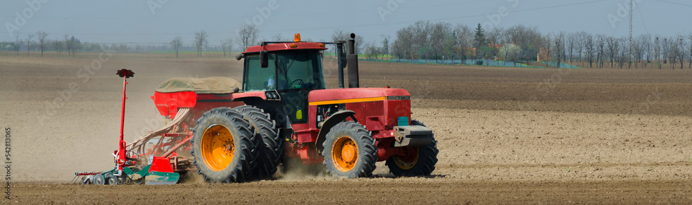 Red tractor sowing on the agricultural field on a sunny spring day Red tractor sowing on the agricultural field on a sunny spring day